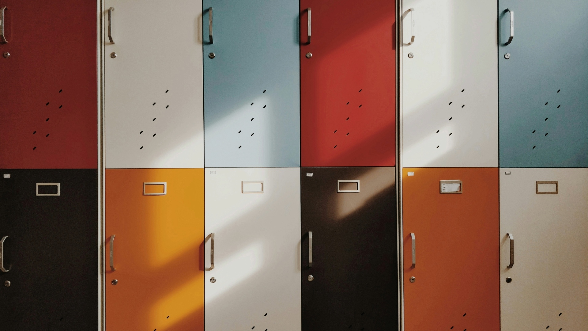 A vibrant, multicolored row of school lockers with sunlight casting diagonal shadows, evoking a university or storage theme.